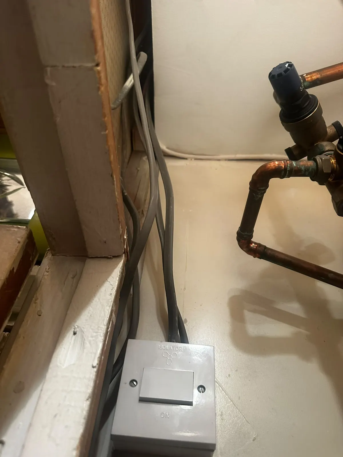 Electrical isolator and surface-run cables beside pipework in a cupboard.