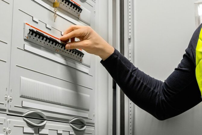 Male Electrician Checking Electric Fuse Board In Server Room